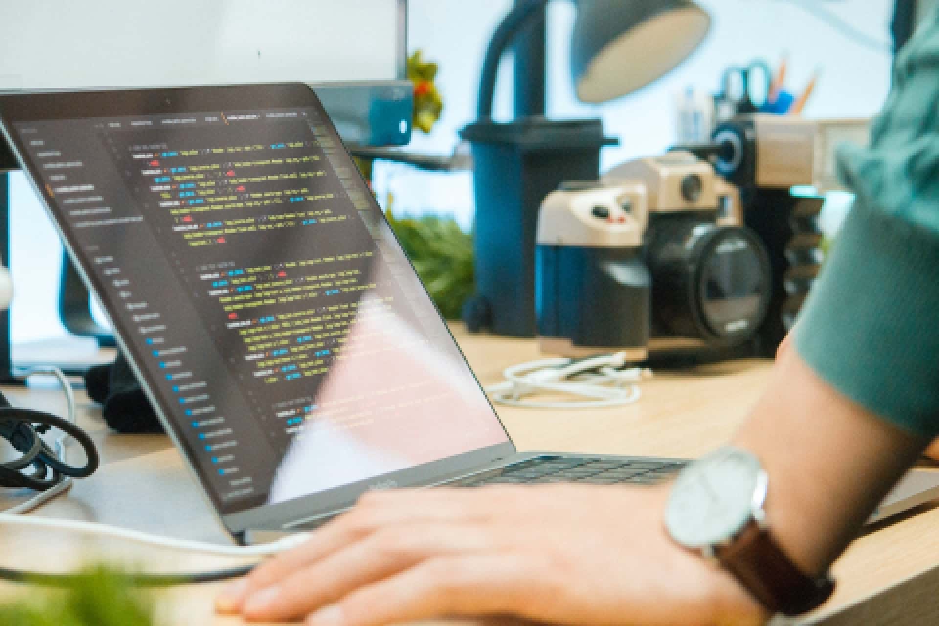 Laptop on a table, behind a human hand, in front of a camera.